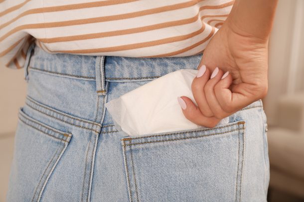 Donna con perdite marroni dopo il ciclo che mette l’assorbente mestruale usa e getta nella tasca dei jeans in casa