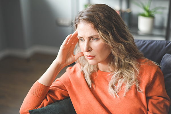 Donna matura seduta sul divano con sintomi come problemi di concentrazione che valuta di sottoporsi a degli esami utili in menopausa