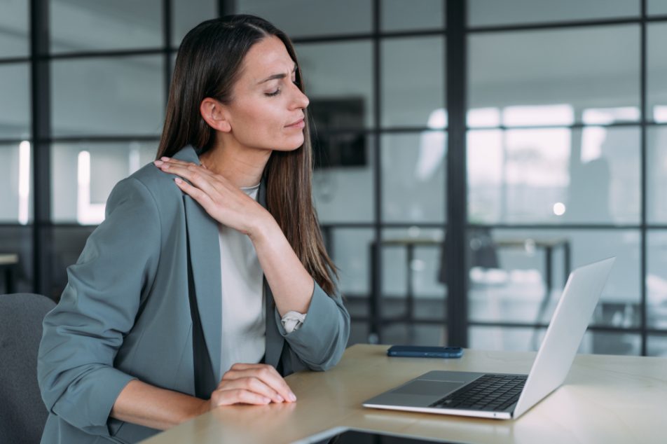 Donna nel suo ufficio che soffre di tensione muscolare, tra i sintomi fisici dell’ipertensione emotiva