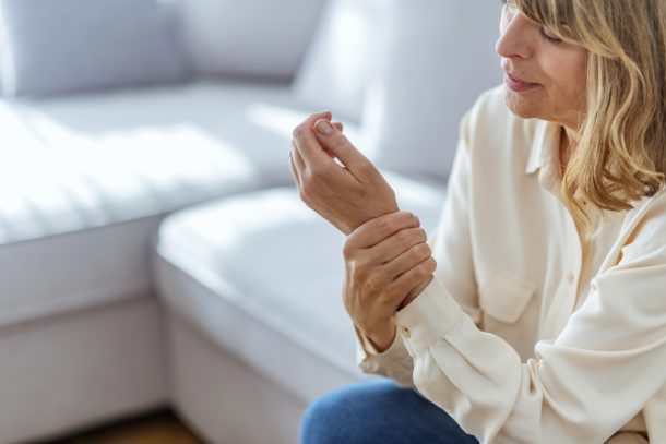 Donna sul suo divano si tiene la mano che trema, tra i sintomi del tremore da stress trema,