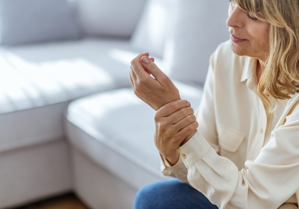 Donna sul suo divano si tiene la mano che trema, tra i sintomi del tremore da stress trema,