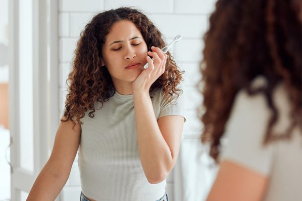 donna-davanti-allo-specchio-avvertendo-sintomi-di-malocclusione-dentale Donna davanti allo specchio del bagno, mentre lava i denti, che avverte dolori gengivali, uno dei sintomi della malocclusione dentale