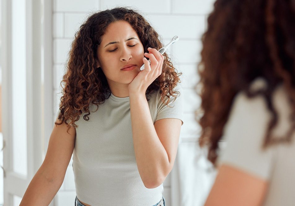 Donna davanti allo specchio del bagno, mentre lava i denti, che avverte dolori gengivali, uno dei sintomi della malocclusione dentale