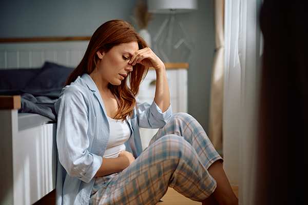 Donna in camera da letto seduta sul pavimento dopo essersi svegliata col mal di pancia, mentre si domanda quanto durerà il suo spotting da stress