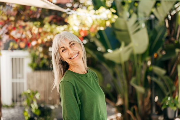donna-in-giardino-adottando-stile-di-vita-sano-per-livelli-progesterone-menopausa Donna in menopausa sorridente nel giardino di casa che adotta uno stile di vita sano mantenendo livelli di progesterone adatti alla sua età