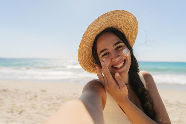 donna-in-spiaggia-applicando-crema-topica-al-cortisone-e-sole Giovane donna in spiaggia che applica sul viso una crema topica a base di cortisone mentre si espone ai raggi solari