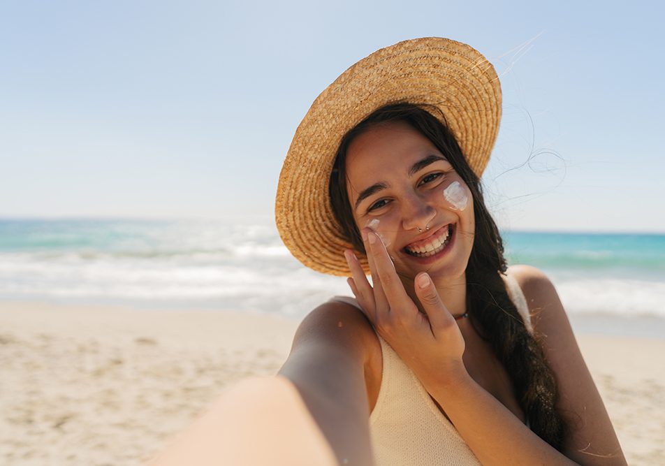 donna-in-spiaggia-applicando-crema-topica-al-cortisone-e-sole Giovane donna in spiaggia che applica sul viso una crema topica a base di cortisone mentre si espone ai raggi solari
