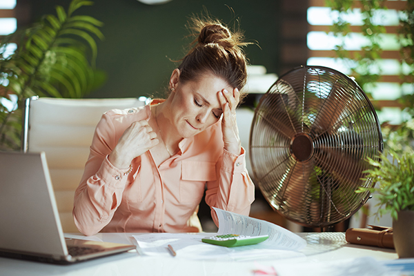 Donna in ufficio seduta accanto ad un ventilatore che non riesce a tollerare il caldo, manifestando sintomi di TSH basso