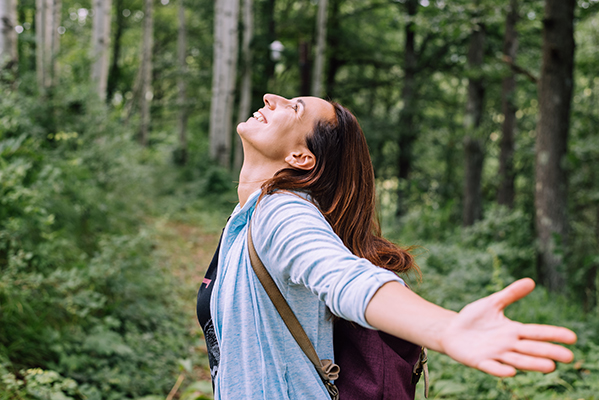 Donna che indossa uno zaino in spalla ed è felice di camminare nel bosco, immersa nella natura