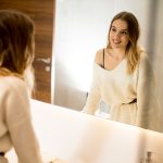 Giovane donna che osserva il suo riflesso allo specchio nel bagno di casa, mentre si occupa delle cause della sua dermatite