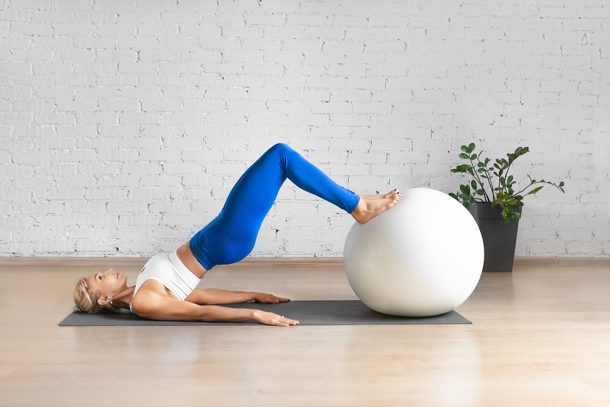 donna-praticando-ginnastica-pelvica-con-fitball Giovane donna caucasica in una spaziosa sala per pilates che pratica ginnastica pelvica con l’ausilio di una fitball