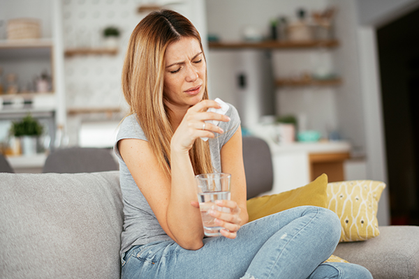 Giovane donna sul divano di casa in posizione leggermente rannicchiata e in cura con la cefixima, che avverte alcuni sintomi collaterali, tra cui disturbi gastrointestinali