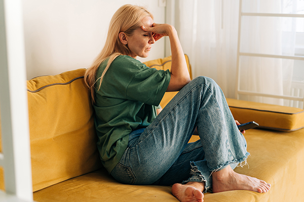 Donna di mezza età accovacciata sul divano che valida il suo stato emotivo per imparare come gestire efficacemente la sua ansia
