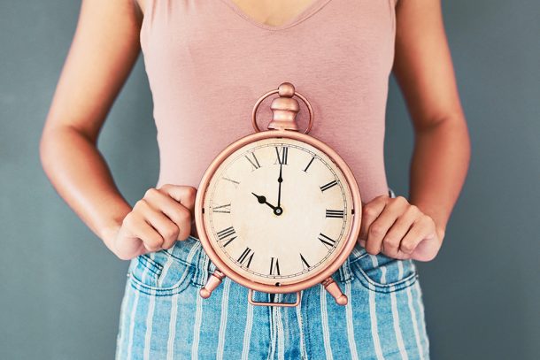 Donna con abiti trendy che tiene sul suo grembo un orologio da tavolo per segnalare il problema del ritardo del suo ciclo mestruale e interrogandosi sulle possibili cause