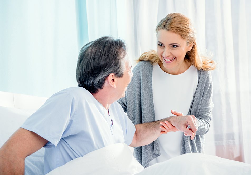 donna-visitando-marito-dopo-trapianto-midollo-osseo Donna in ospedale che fa visita al marito, aiutandolo a stare alzato nel letto in seguito al trapianto di midollo osseo