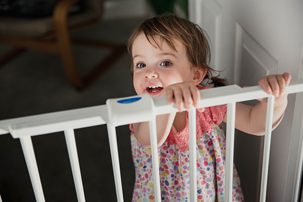 Piccola fanciulla sorridente dietro a un cancelletto di sicurezza in casa, installato dai genitori per la prevenzione degli incidenti nei bambini dovuti ad episodi di sonnambulismo