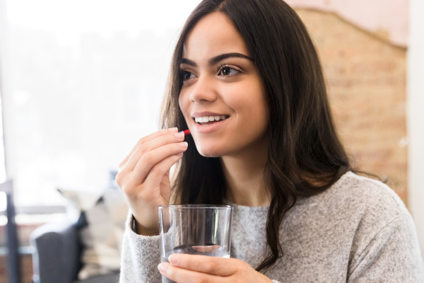 Giovane donna con un bicchiere d'acqua in mano assume le benzodiazepine in compresse