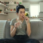 Giovane donna con bicchiere d'acqua in mano assume betametasone per malattia dermatologica