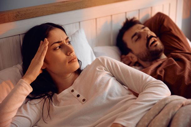 in-camera-da-letto-con-donna-sveglia-e-uomo-con-apnee-ostruttive-del-sonno Una coppia in camera da letto all’alba, di cui la donna non riesce a riposare a causa dell’uomo con apnee ostruttive del sonno