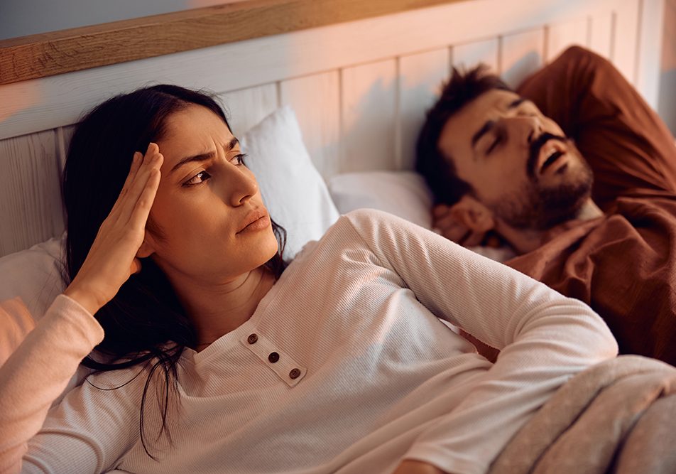 in-camera-da-letto-con-donna-sveglia-e-uomo-con-apnee-ostruttive-del-sonno Una coppia in camera da letto all’alba, di cui la donna non riesce a riposare a causa dell’uomo con apnee ostruttive del sonno