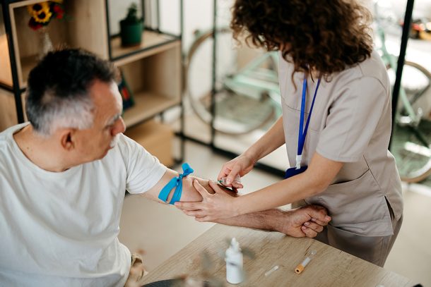 Infermiera che preleva il sangue al paziente maturo presso la sua abitazione; egli ha i trigliceridi bassi e il colesterolo alto