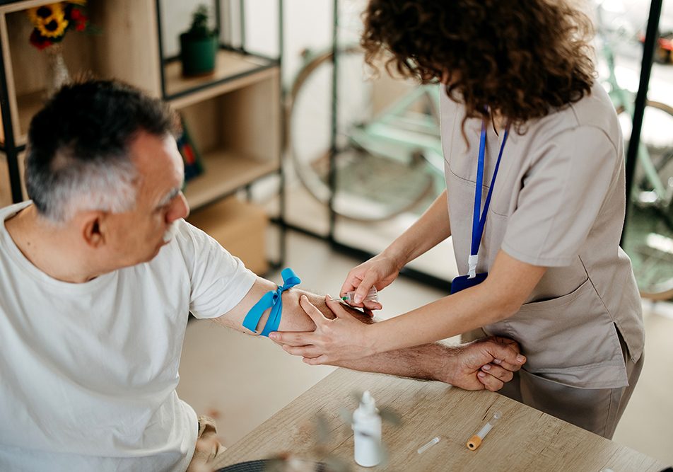 Infermiera che preleva il sangue al paziente maturo presso la sua abitazione; egli ha i trigliceridi bassi e il colesterolo alto
