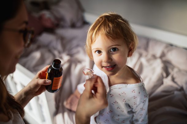 madre-somministrando-cefixima-bambini Madre che somministra alla bambina sorridente, adagiata sul letto della sua cameretta, la cefixima prescritta dal pediatra