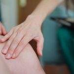 Medico a domicilio che visita una paziente donna con la trombosi venosa profonda, toccandole delicatamente l’area delle gambe