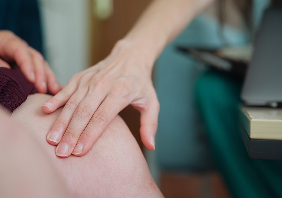 Medico a domicilio che visita una paziente donna con la trombosi venosa profonda, toccandole delicatamente l’area delle gambe