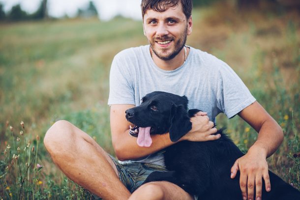 Padrone seduto in un prato in compagnia suo cane, un labrador retriever nero, prendendosi cura della sua leishmaniosi