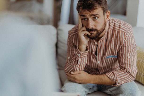 Paziente con sintomi d’ansia generalizzata, con uno sguardo leggermente preoccupato, seduto sul divano mentre si sottopone ad una seduta di psicoterapia