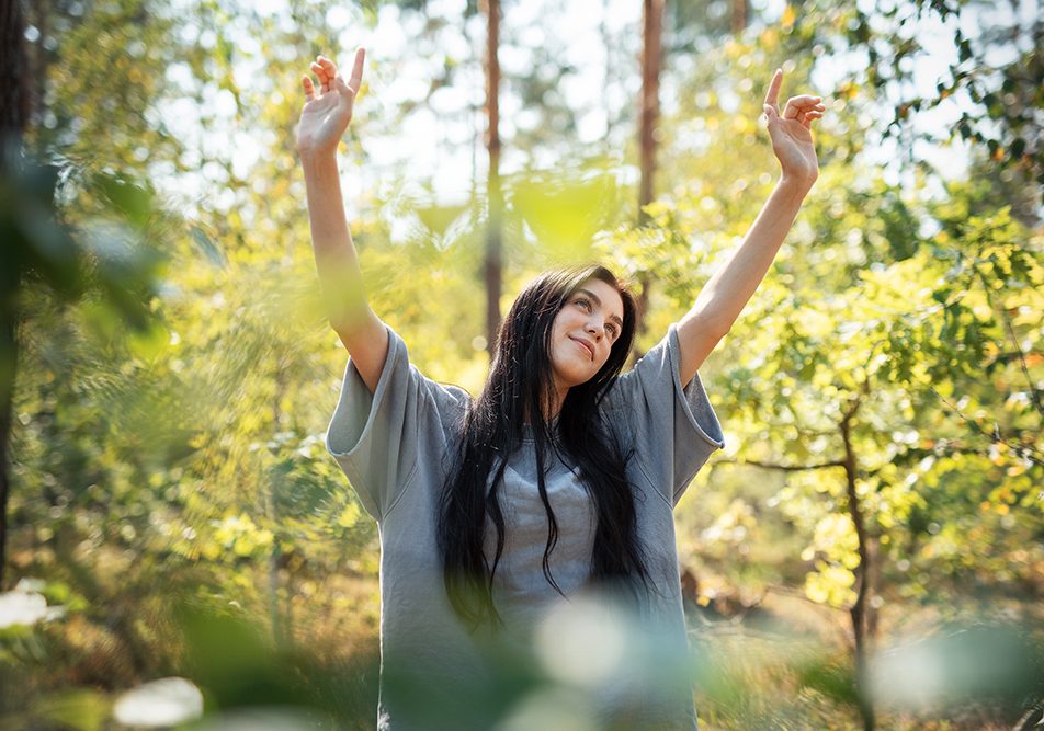 Ragazza nella foresta serena e rilassata mentre respira aria fresca, migliorando il suo contatto con la natura e il benessere