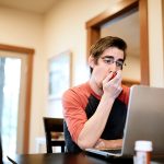 Uomo a casa davanti al computer che utilizza un inalatore per poter gestire i sintomi della fibrosi cistica