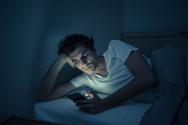 Giovane uomo che usa dispositivo elettronico prima di dormire, tra le cause dei disturbi del sonno