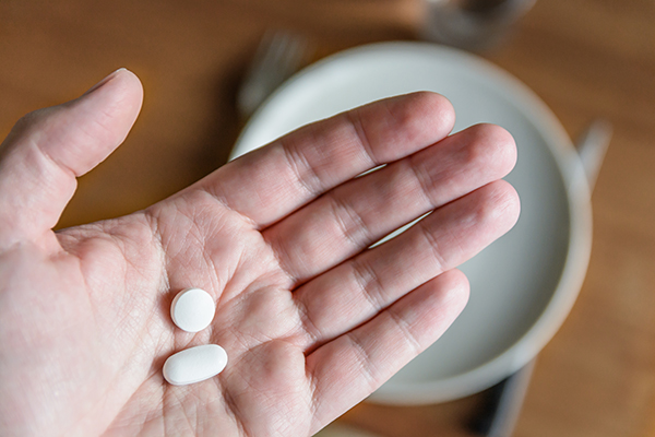 Uomo che tiene nel palmo della mano due farmaci differenti, interrogandosi su se si possono prendere cortisone e antinfiammatori insieme