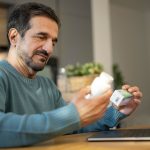 Uomo seduto davanti al computer portatile che legge le confezioni di ketoprofene e cortisone per verificare se è corretto assumerle insieme