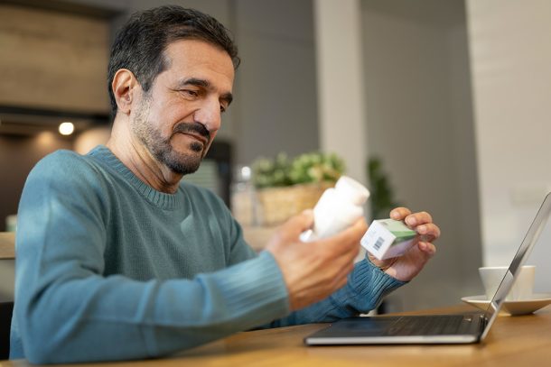 uomo-leggendo-confezioni-ketoprofene-e-cortisone-insieme-per-verificare-assunzione Uomo seduto davanti al computer portatile che legge le confezioni di ketoprofene e cortisone per verificare se è corretto assumerle insieme