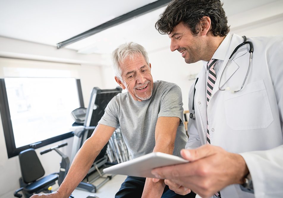 uomo-maturo-sottoponendosi-a-visita-medico-sportiva-non-agonistica Uomo maturo in un centro di medicina dello sport in compagnia del medico che si sottopone a una visita medico sportiva non agonistica, per poter praticare attività fisica in salute e sicurezza