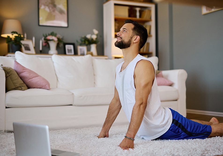 uomo-sul-tappeto-allungando-colonna-vertebrale-attraverso-esercizi-mal-di-schiena Uomo sul tappeto, con davanti il suo laptop, sollevato dall’allungamento della colonna vertebrale attraverso esercizi mirati per il mal di schiena