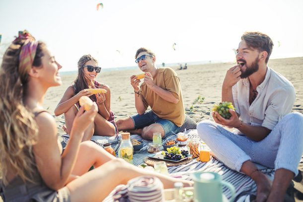 Amici durante un picnic sulla spiaggia, che consumano alimenti freschi e leggeri per evitare i sintomi della gastrite
