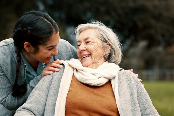 Caregiver familiare che passeggia insieme alla donna anziana in sedia a rotelle nel giardino di casa