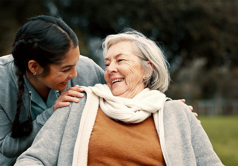 Caregiver familiare che passeggia insieme alla donna anziana in sedia a rotelle nel giardino di casa