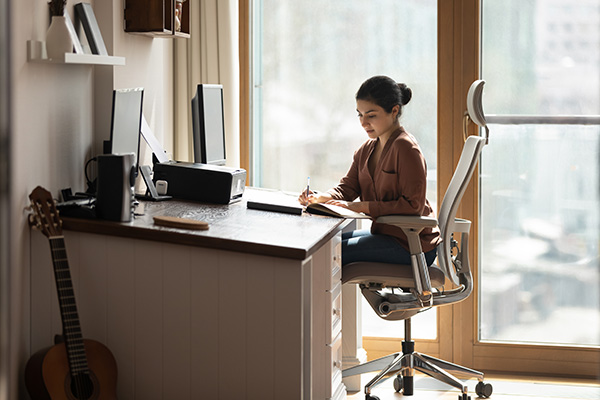 Donna seduta alla scrivania sostenuta da una sedia ergonomica, che rispetta il principio di salute in ambiente di lavoro