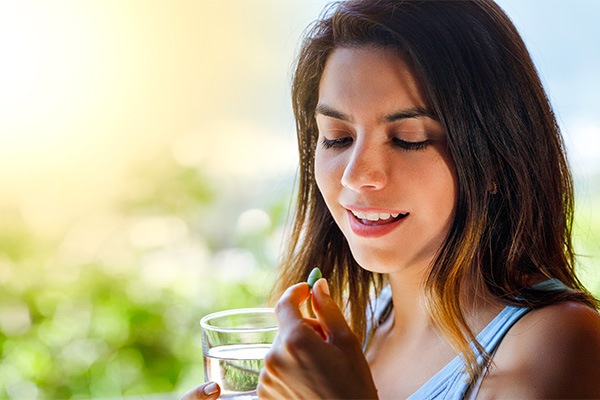 Donna all’aperto che assume degli integratori per capelli insieme ad un bicchiere d’acqua