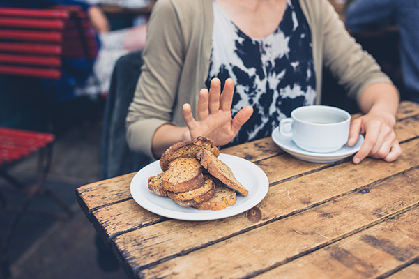 Donna con celiachia e gonfiore addominale nel dehors di un bar che rifiuta di mangiare del pane integrale