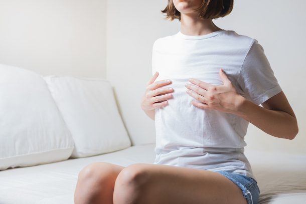 donna-con-dolore-capezzolo-toccandosi-seno Giovane donna seduta sul divano di casa che si tocca il seno in quanto avverte dolore al capezzolo