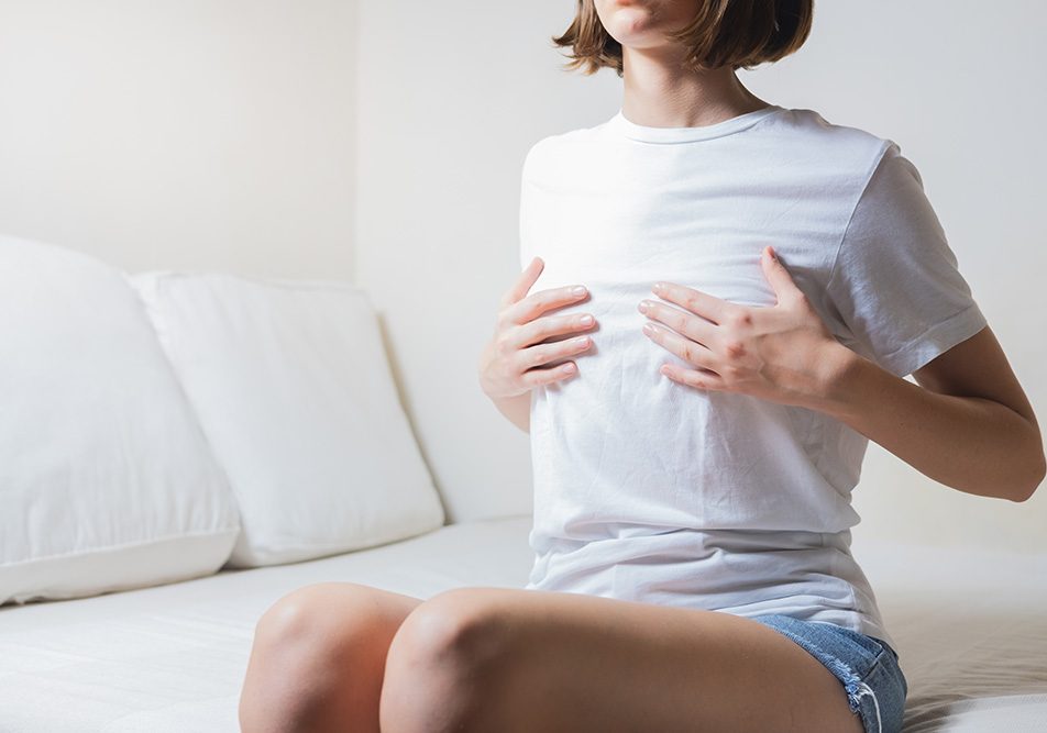 donna-con-dolore-capezzolo-toccandosi-seno Giovane donna seduta sul divano di casa che si tocca il seno in quanto avverte dolore al capezzolo