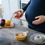 Donna con celiachia e disturbi ginecologici che ha voglie di cibo durante la gravidanza e seleziona dal tavolo una macedonia di frutta