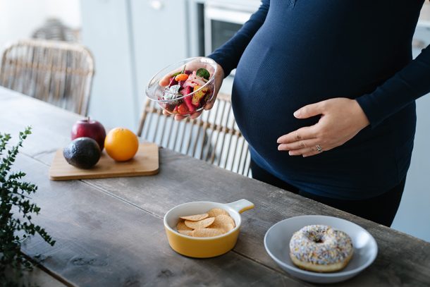 donna-incinta-con-celiachia-e-disturbi-ginecologici-avendo-voglie Donna con celiachia e disturbi ginecologici che ha voglie di cibo durante la gravidanza e seleziona dal tavolo una macedonia di frutta