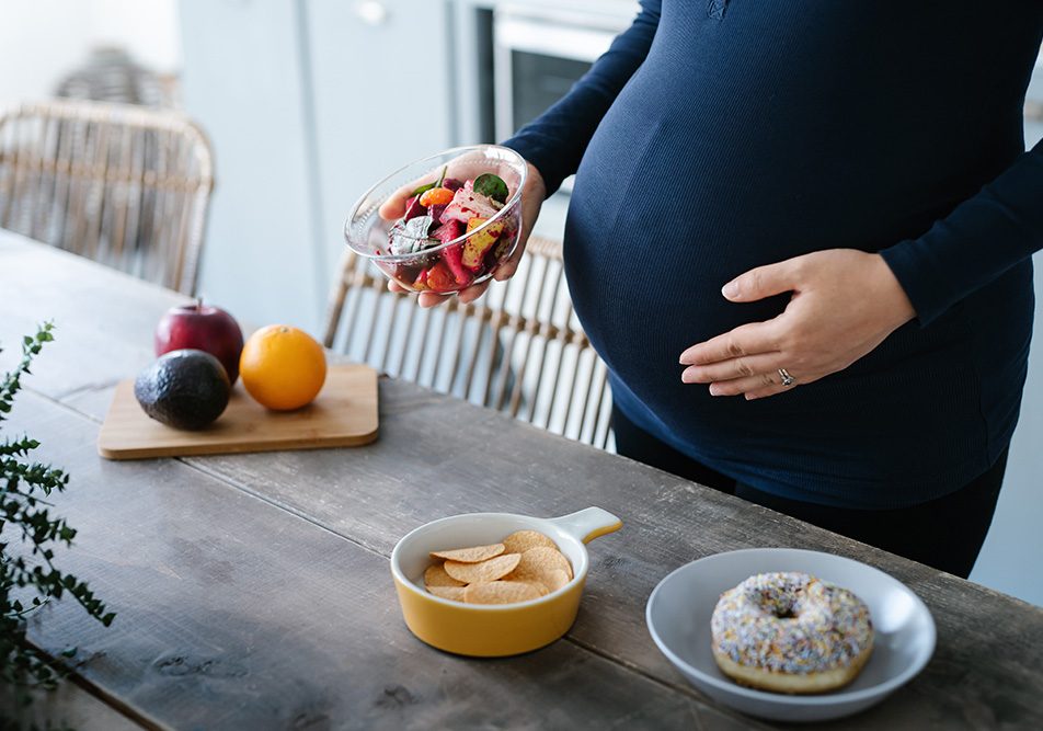 donna-incinta-con-celiachia-e-disturbi-ginecologici-avendo-voglie Donna con celiachia e disturbi ginecologici che ha voglie di cibo durante la gravidanza e seleziona dal tavolo una macedonia di frutta